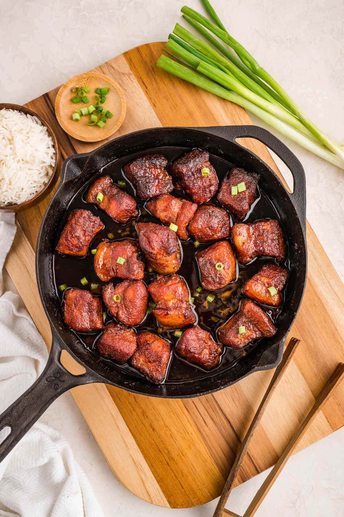 top down view of the pork belly burnt ends in a cast iron skillet with green onion and rice to accompany it.