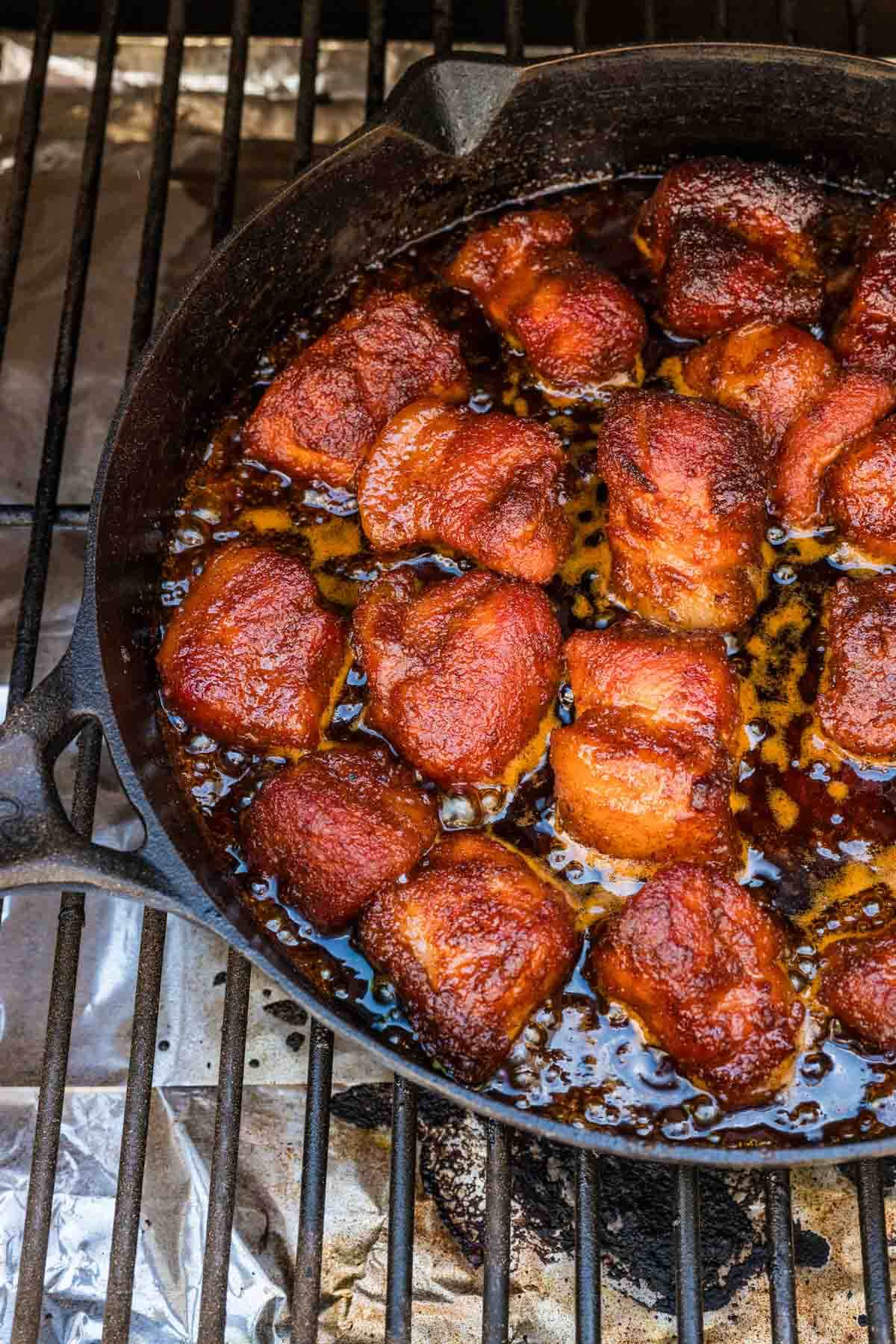 skillet of the smoked pork belly burnt ends on the grill and protected with aluminum foil.