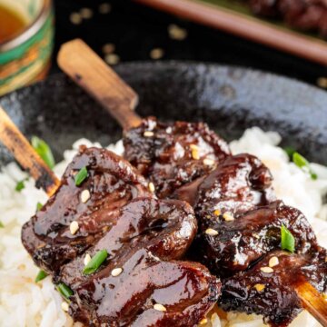 two bamboo skewers with grilled chicken hearts over a bed of rice with Japanese tea in the background.