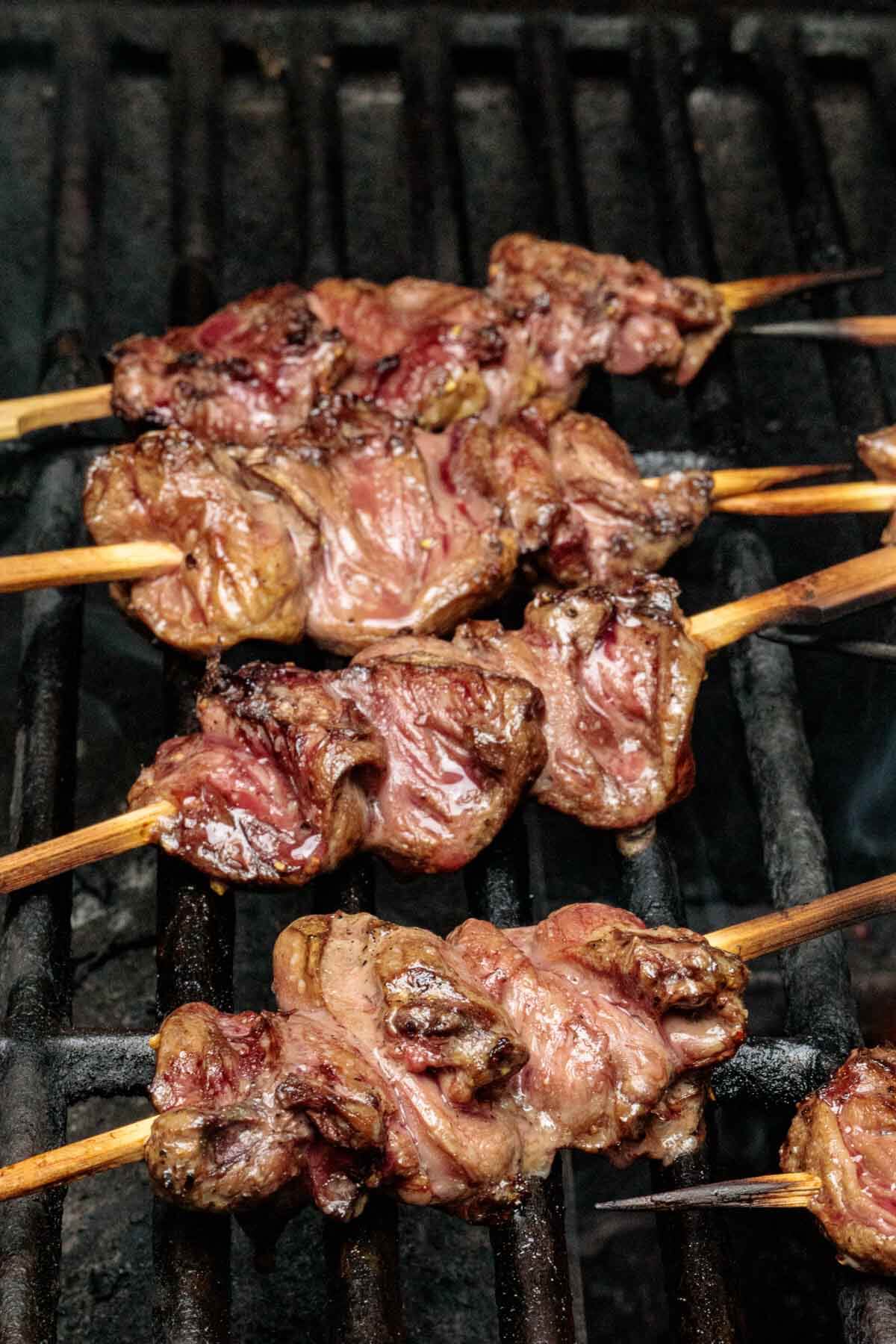 several chicken hearts butterflied and skewered onto bamboo skewers and on the hot grill.