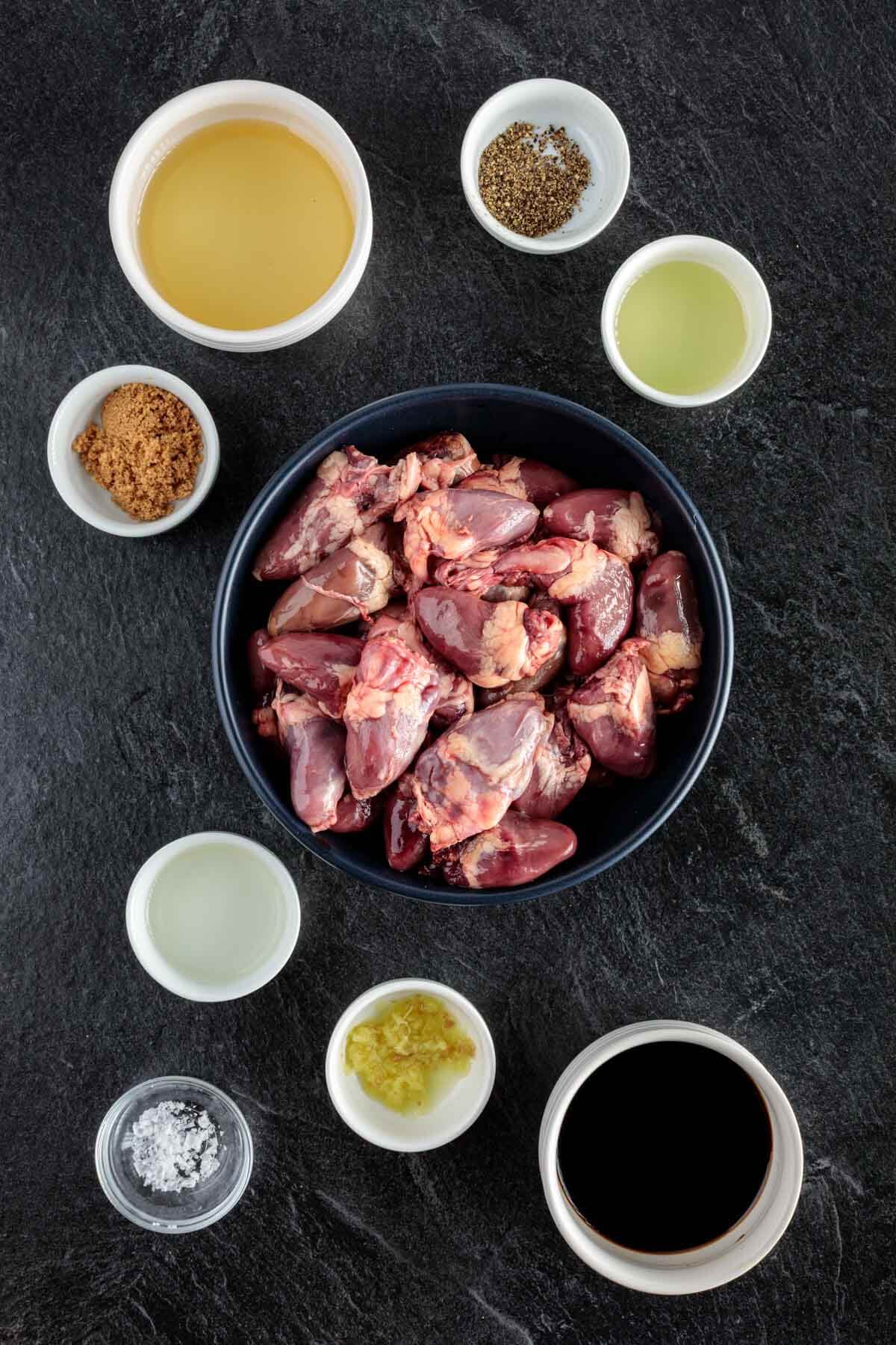 top down view of a bowl of chicken hearts and ramekins with the seasonings and spices needed for this recipe.