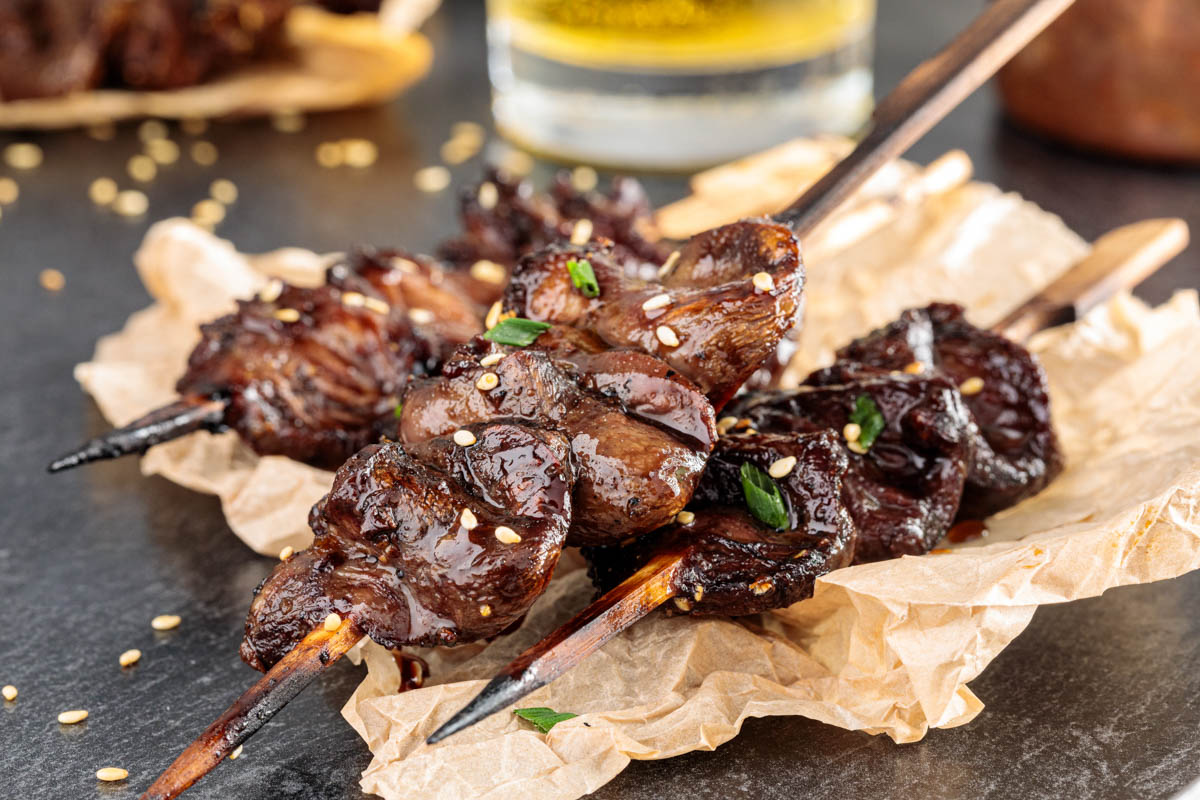 several skewers loaded with grilled chicken hearts on butcher paper.